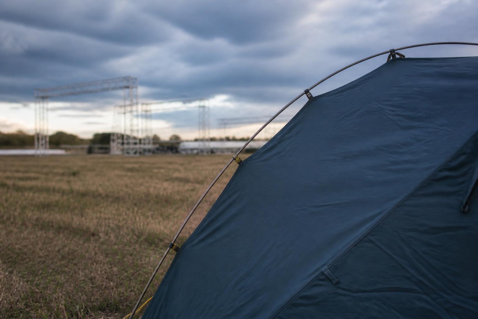 un champ breton transformé en site de festival, scène et structures métalliques au loin sous un ciel changeant